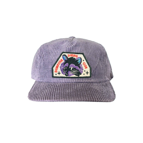 Lilac corduroy hat with a raccoon patch. Patch reads "dumpster diving crew"