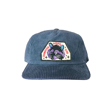 Steel blue corduroy 5-panel hat. It has a raccoon patch that reads "dumpster diving club"