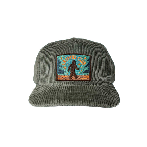 Green corduroy cap with a patch featuring a bigfoot and 'Cryptid Club' text on a white background