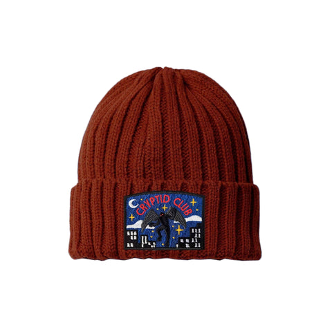 Rust beanie with a mothman "Crypid Club" patch on the cuff