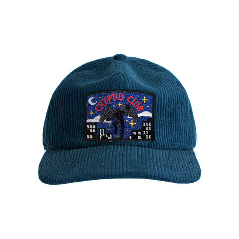 Turquoise corduroy cap with a Mothman 'Cryptid Club' patch on a white background