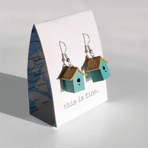 Image shows two teal birdhouse-shaped earrings hanging from silver wires