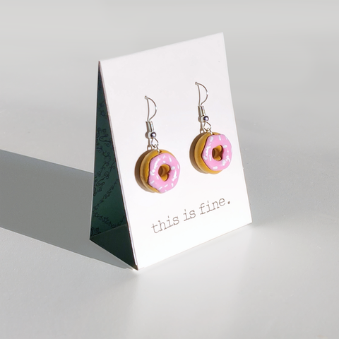 Image shows a pair of pink sprinkled doughnuts hanging from silver wires.