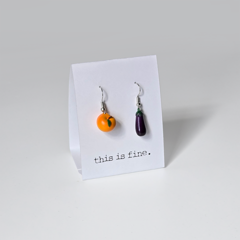 Image shows a pair of earrings hanging from silver wires. One is a peach, and one is an eggplant.