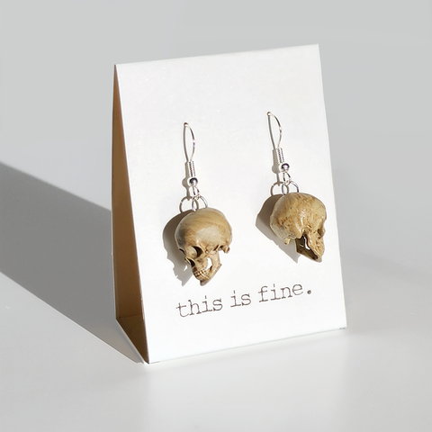 Image shows a pair of realistic skull-shaped earrings hanging from silver wires
