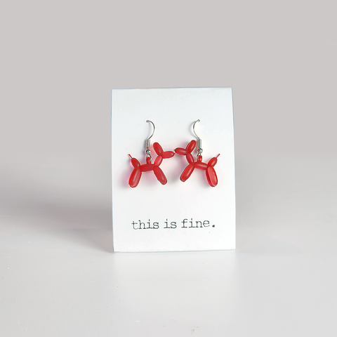 Image shows a pair of earrings in the shape of a red balloon dog. They hang from silver wires.