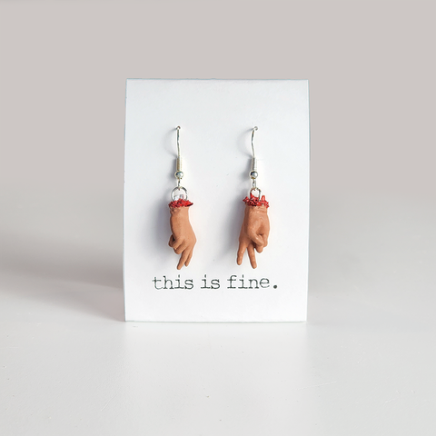 Image shows a pair of earrings hanging from silver wires. They are severed hands showing the peace sign.