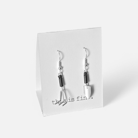 Image shows a pair of earrings hanging from silver wires. One is a trowel, and one is a hand rake.