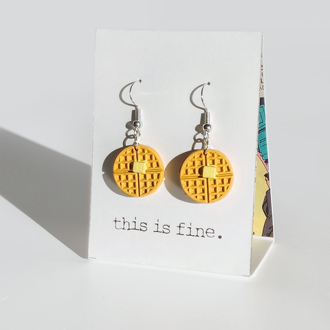 Image shows a pair of earrings hanging from silver wires. They are waffles with a pad of butter.