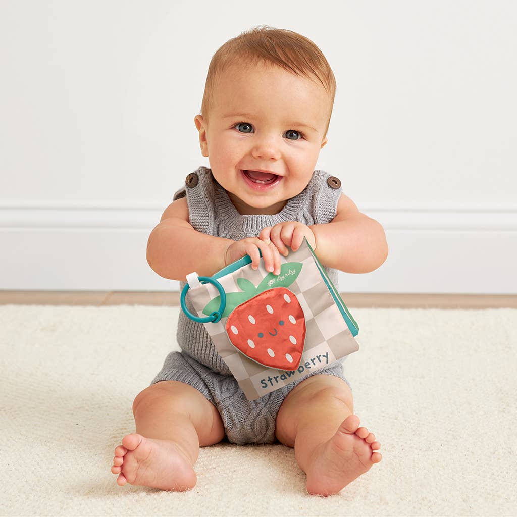 Image shows a baby holding a fabric book with a strawberry on the front