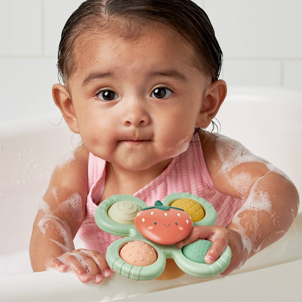 Image depicts a baby covered in suds playing with the toy in the bath