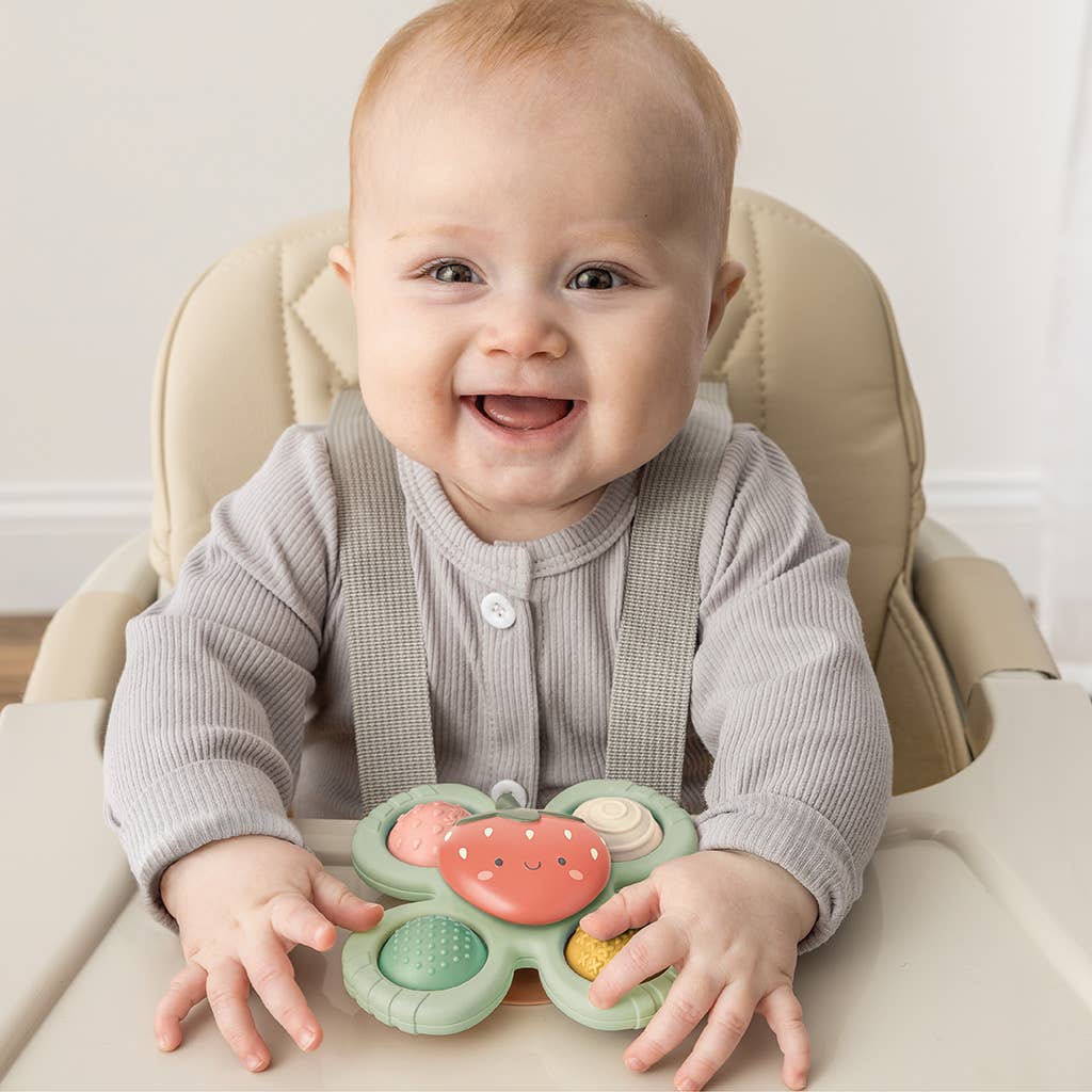 Image depicts a smiling baby playing with the toy at its highchair 