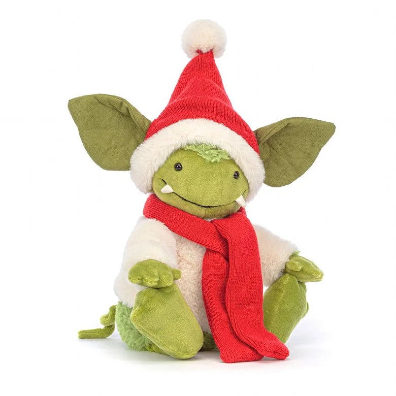 A stuffed green gremlin with large ears and small fangs. Its wearing a white sweater, Santa hat, and red scarf.