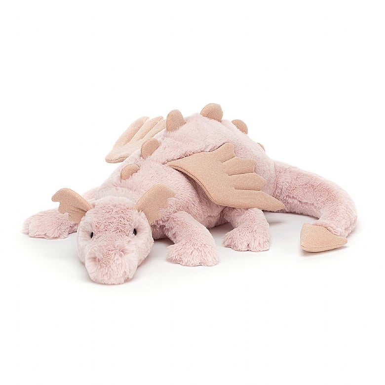 A light pink stuffed dragon with peach-colored sparkly ears, spikes, wings, and tail tip. The dragon is laying down.