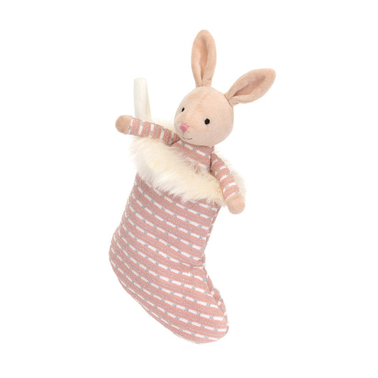 A stuffed bunny inside of a stocking. The bunny is wearing pink shimmering pajamas that match the outside of the stocking.