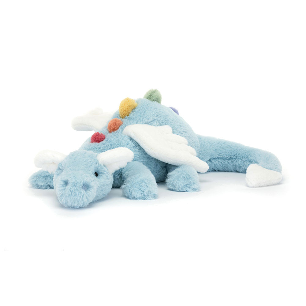 A light blue stuffed dragon. The dragon is laying down. Its wings, ears, and tail tip are sparkly white. Its spikes are rainbow.