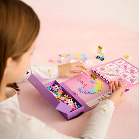 Child playing with a colorful puzzle set on a pink surface. She is building a unicorn.