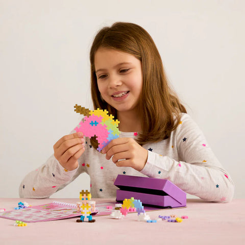 Young girl playing with colorful building blocks on a pink table.