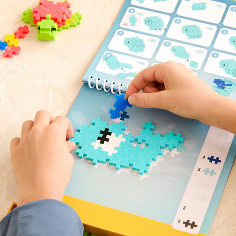 Children's hands playing with a pixelated whale puzzle on an educational mat.