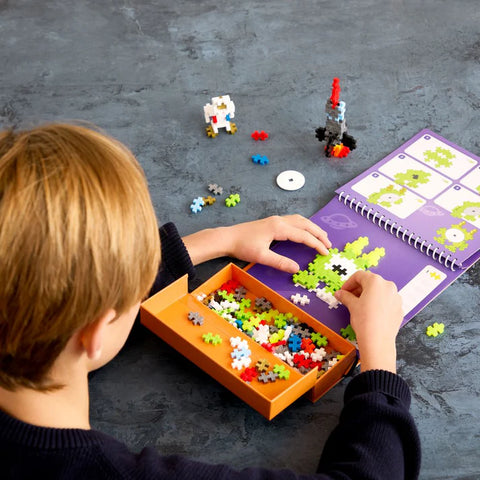 Child playing with colorful building blocks and a purple activity book on a gray surface