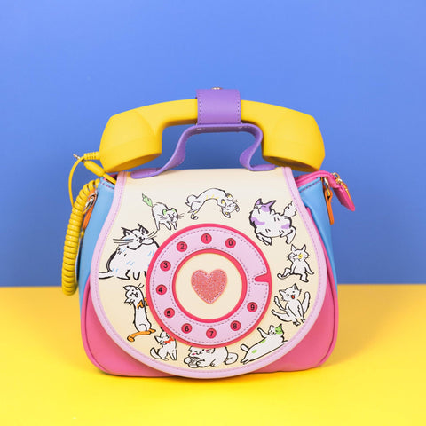Image shows a handbag with a yellow phone on top. It shows various cats in a circle around a pink rotary dial.
