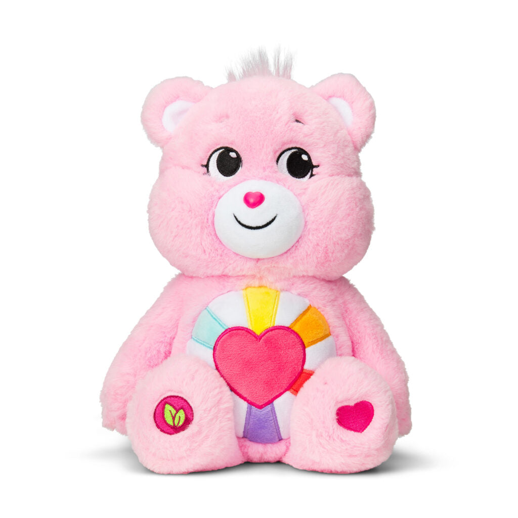 Image shows the Care Bear Hopeful Heart Bear. It is a light pink bear with a heart on its belly, with sun rays extending from the heart.