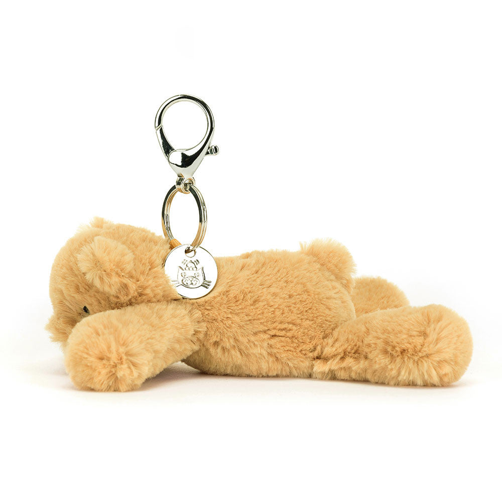 The side view of A floppy tan teddy bear hanging from a clip keychain