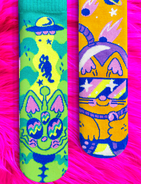 Image shows a pair of mismatched socks. One is a green alien cat, and one is an orange astronaut cat.