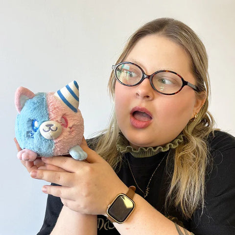 A woman holds the plush cotton candy themed kitty near her face. It is slightly smaller than her head.