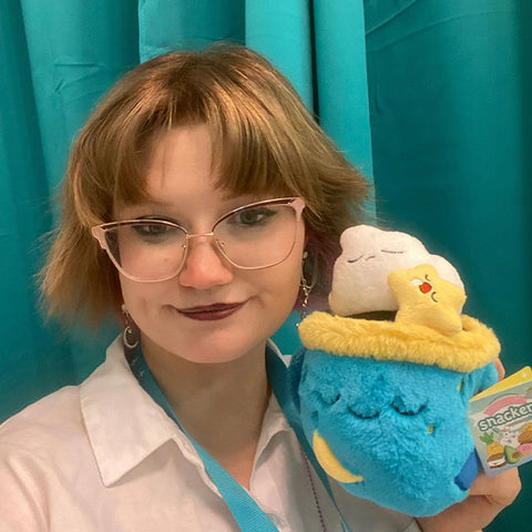 A woman holds the plush coffee cup near her face. It is slightly larger than her head.