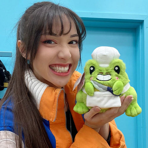 A woman holds the plush chef frog near her face. It is slightly smaller than her head.
