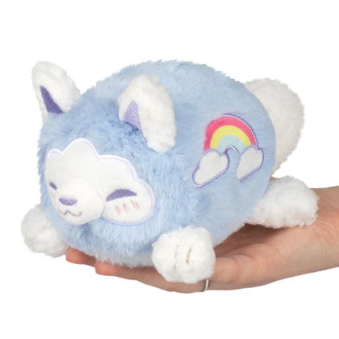 A pale blue stuffed Kitsune held in an adult's hand. It has an embroidered rainbow on its side.