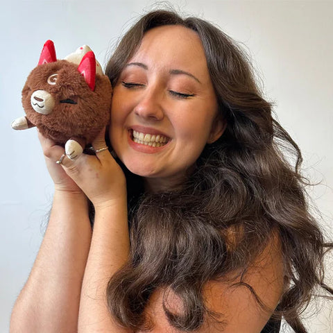 A woman holding the stuffed cocoa-themed kitsune. It is slightly smaller than her head.