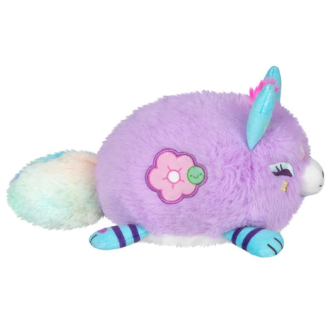 A side view of the lavender stuffed kitsune. It has a round body, and an embroidered flower on its side.