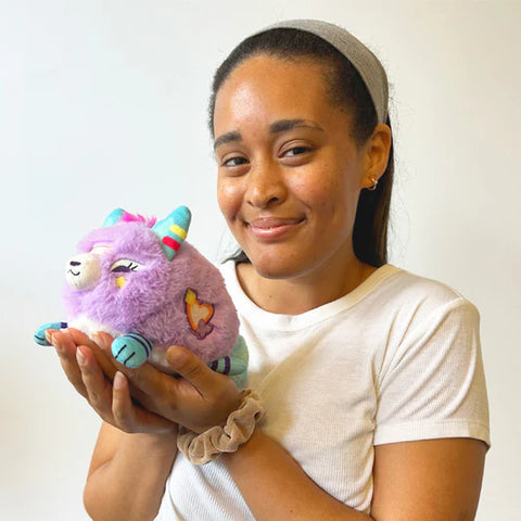 A woman holding the lavender stuffed kitsune. It is slightly smaller than her head.