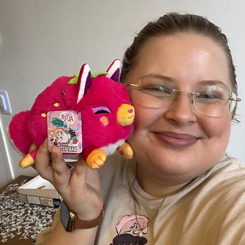 A woman holds the stuffed fruity kitsune. It is slightly smaller than her head.