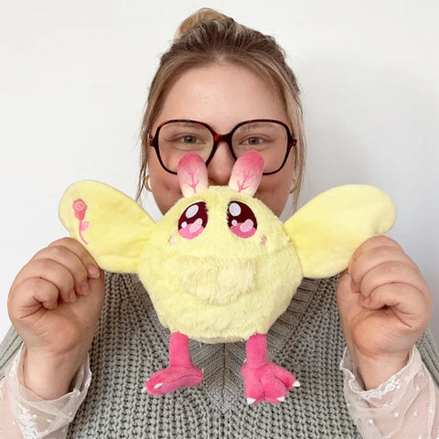 A woman holds the plush maple rosy mothman near her face. It is slightly smaller than her head.