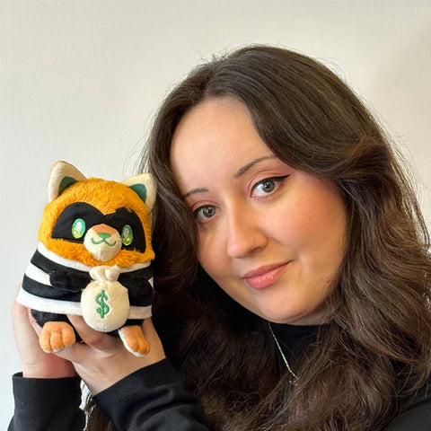 A woman holds the plush burglar kitty near her face. It is slightly smaller than her head.