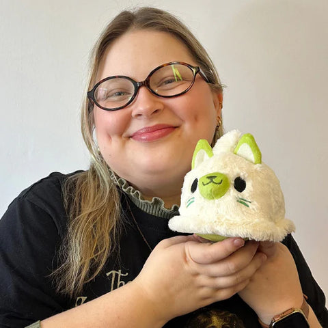 A woman holds the plush ghost kitty near her face. It is slightly smaller than her head.