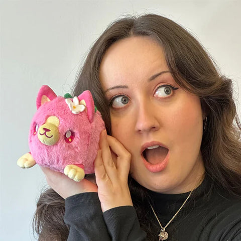 A woman holds the plush strawberry kitty near her face. It is slightly smaller than her head.