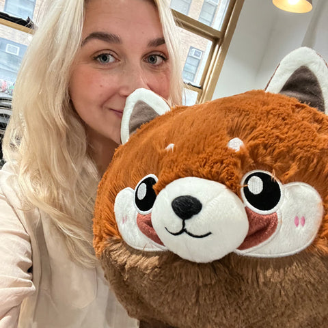 A woman holds the plush red panda. It is about the size of her torso.