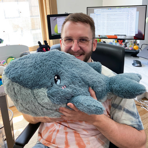 A man holds the plush blue whale. It is about the size of his torso.