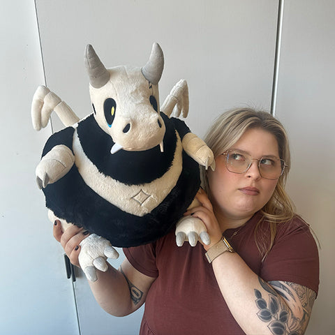 Image shows a woman holding the stuffed bone dragon. It is much larger than her head.