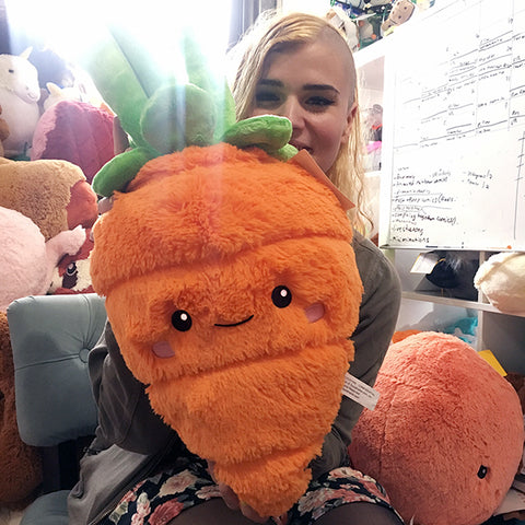 A woman holds the plush carrot. It is about the size of her torso.