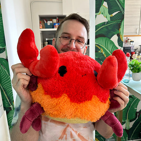 A man holds the plush crab with its claws open. It is about the size of his torso.