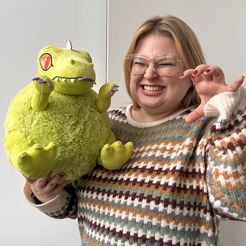 A woman holds the plush Reptar. It is slightly larger than her chest.