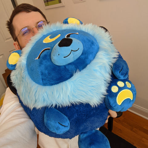 A man holds the plush lunar lion. It is about the size of his torso.