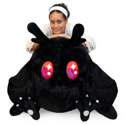 Image shows a massive stuffed Baby Mothman. A woman kneels behind him for size reference.