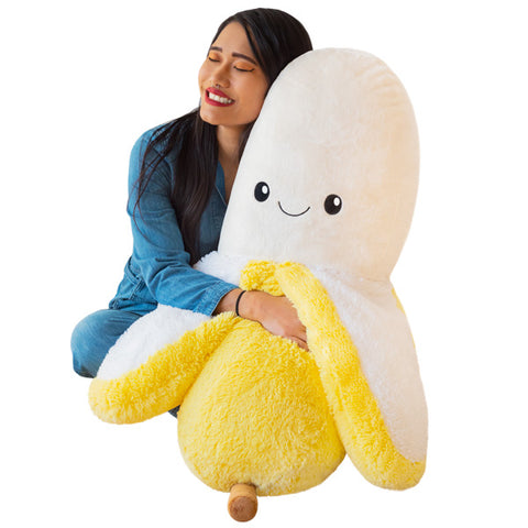 Image shows a woman sitting down and hugging a massive stuffed banana