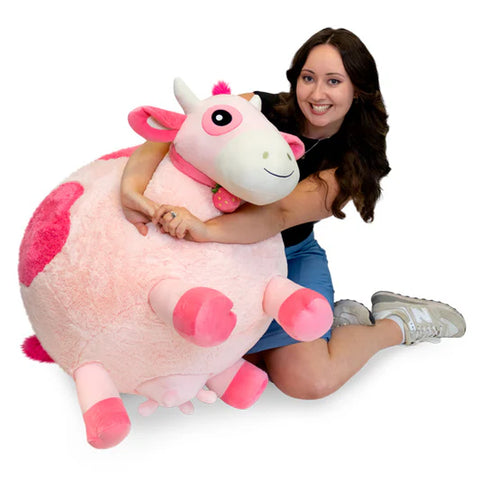 Image shows a woman hugging a massive stuffed pink cow